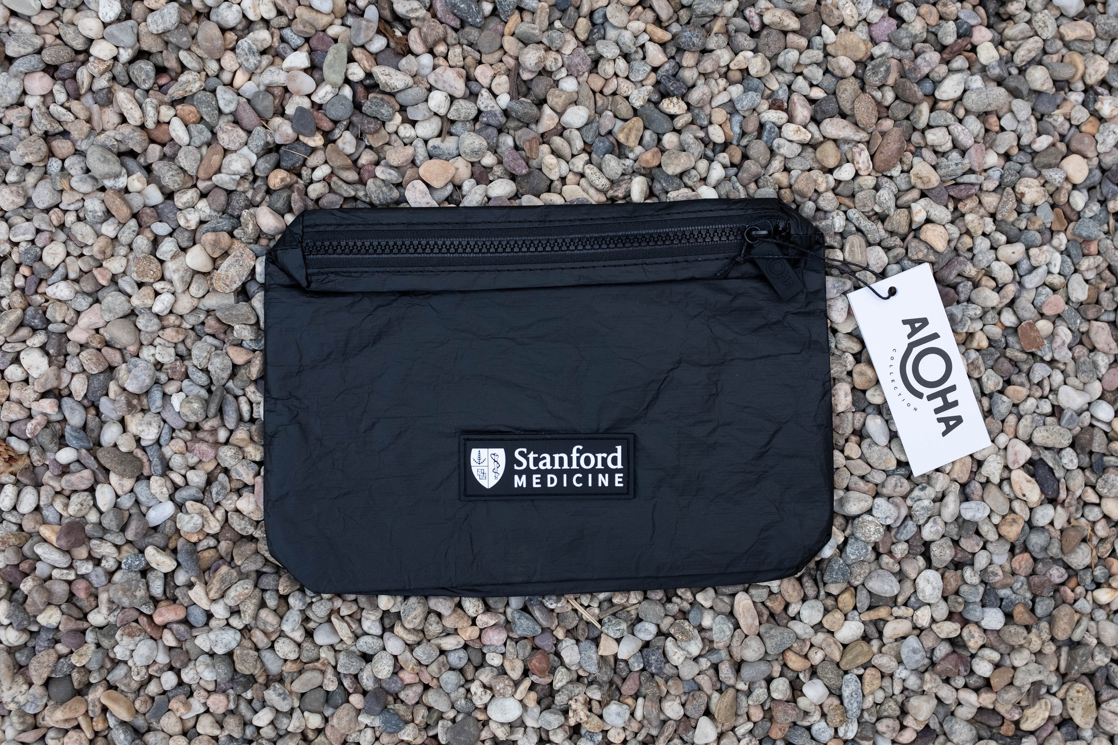 Stanford Medicine branded Aloha pouch laid flat on gravel with hang tag