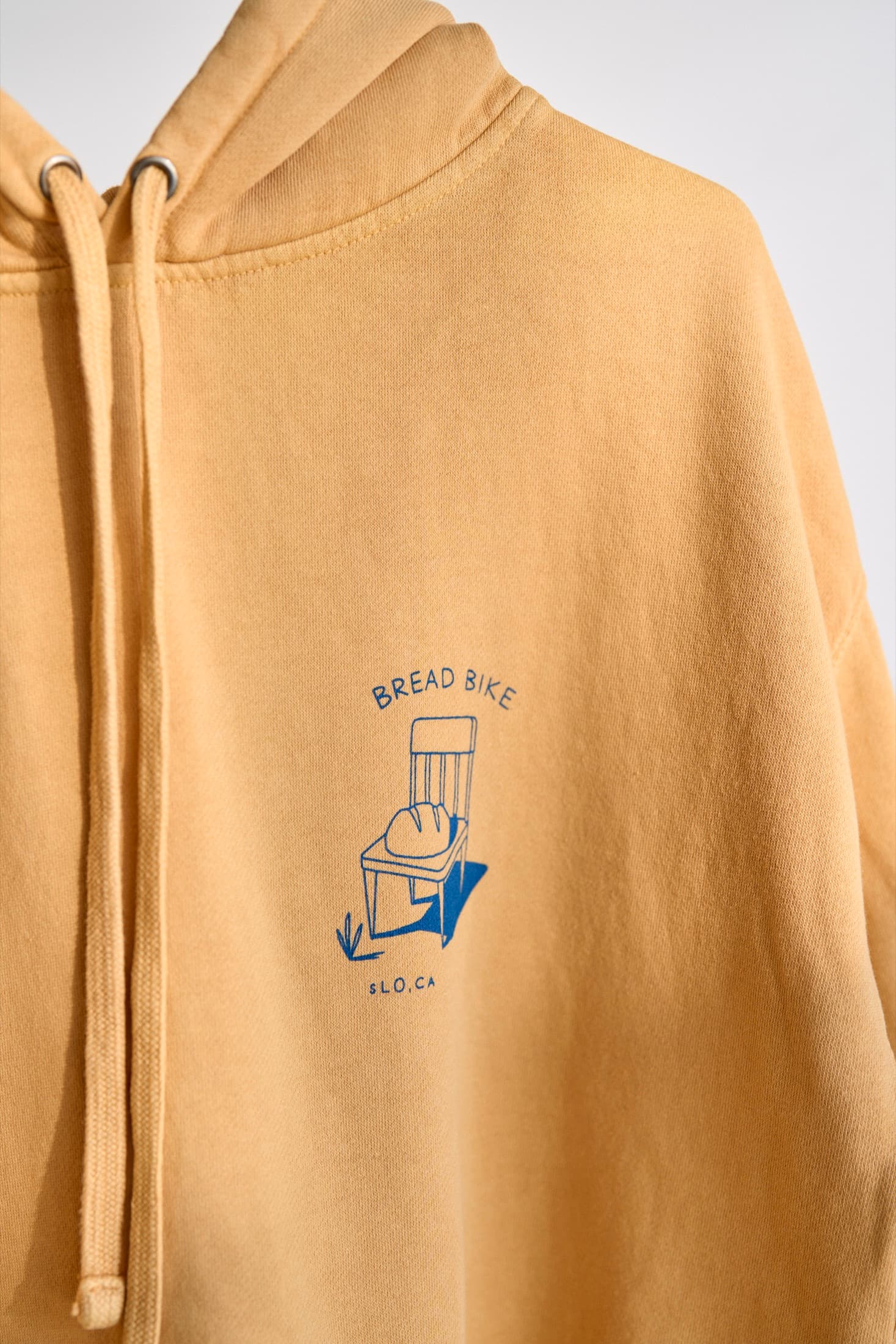 Close detail of a yellow hoodie with a small blue chest print shown as the Waterbased Ink finishing example